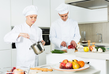 Professional chefs  in uniform  working with vegetables on kitchen