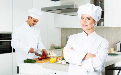 Two cheerful woman and man young chefs preparing food with paper recipe on kitchen