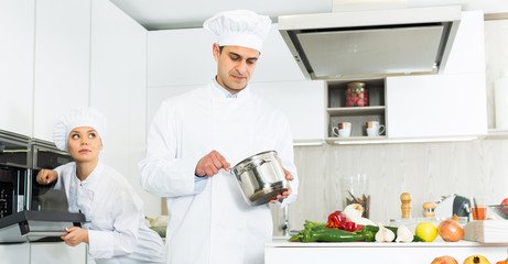 Portrait of the man proffesional who is cooking soup in pot in the kitchen