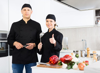 Man and woman kitcheners in uniform are standing with devices in the kitchen