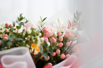 part of a large bouquet of delicate little flowers, in the middle of pink spray roses in focus, around white and yellow flowers out of focus in daylight in bright packaging