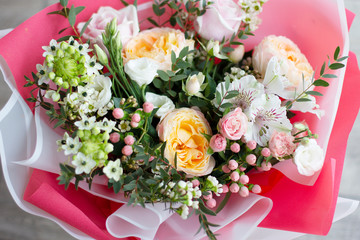 a large bouquet of different flowers of pastel delicate shades: roses, buttercups, eustoma, alstroemeria in bright wrapping paper of pink and white colors, top view