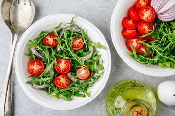 Healthy Green Fresh Arugula Salad Bowl with Tomatoes and Red Onions. Top view