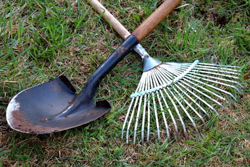 Garden tools, shovel and rake crossed lie on the grass.