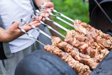 Chief-cooker's hands are grilling BBQ at home on an open fire, skewing metal sticks with juicy slices of meat. Summer picnic in nature