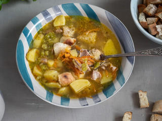 Pea soup in a deep ceramic plate with crackers and a tablespoon, nyato large planos from the top view.