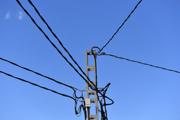Old electric pole and wires in Spain in front of a blue sky.