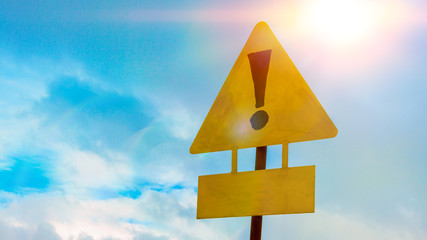 Exclamation point of attention on a yellow triangular sign with a sign for signing. Against the sky in the sunset. Warning, danger.