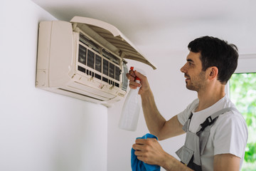worker cleaning home air conditioner with antibacterial spray
