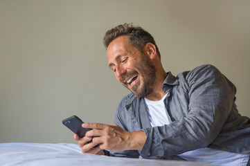 young handsome and happy man at home using internet mobile phone on bed smiling cheerful and...