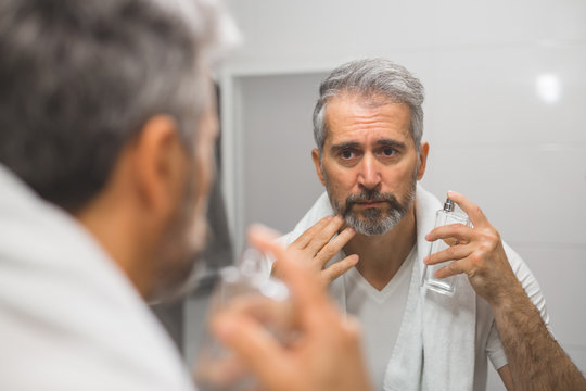 Middle Aged Bearded Gray Haired Man Applying Perfume In Bathroom