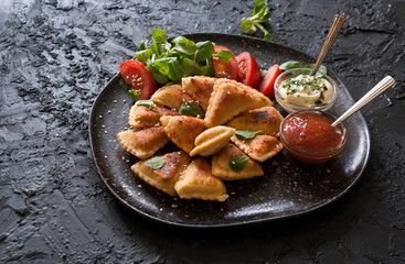 Small puff fried pies with vegetarian and meat fillings served with sauces on a black slate Board