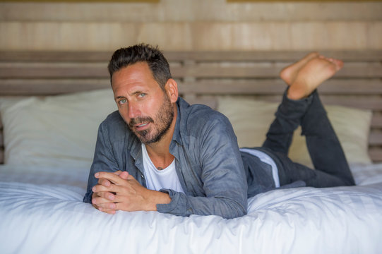 interior portrait of 30s to 40s happy and handsome man at home in casual shirt and jeans lying on bed relaxed at home smiling confident and cool feeling positive