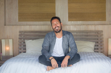 interior portrait of 30s to 40s happy and handsome man at home in casual shirt and jeans sitting on bed relaxed at home smiling confident and happy feeling positive