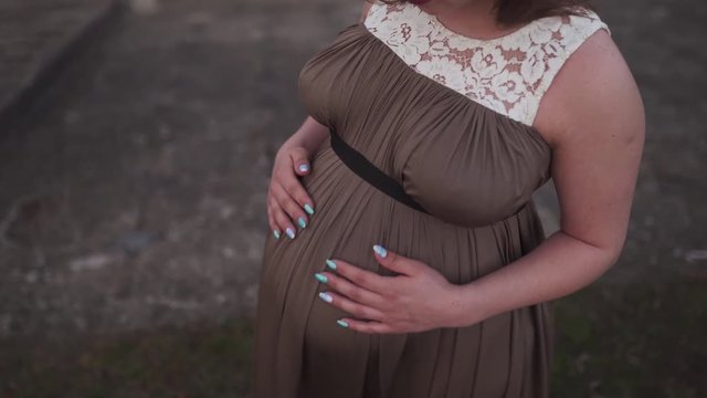 Holding belly close up - Young pregnant woman is happy in her travel destination country Latvia with a view over city Riga and river Daugava - White caucasian girl wearing maternity dress