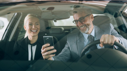 middle aged businessman with his young colleague using cellphone in car