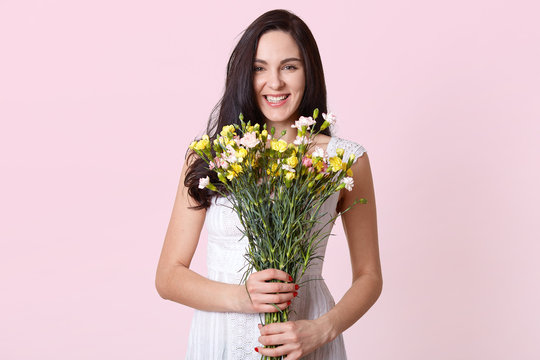 Image of girl holding bouquet of flowers in the hands, chorming lady expresses happyness, looking directly at camera, being in good mood on her birthday. Copy space for promotion or advertisment.