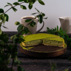 green matcha cheesecake, on a wooden board, cup of coffee on a light grey background, green leaves infant