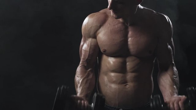 Sporty young man doing exercise with dumbbells on black background. Strong chest and shoulder muscles. Bodybuilding concept