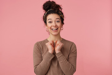 Portrait of a happy young curly girl, smiles broadly, rejoices, putting hands to chest, looking at the camera isolated over pink background.