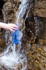 Woman holding a plastic bottle drawing clean water from cold spring.