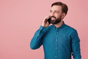 Glad attractive bearded man, looking away and smiling, wearing a denim shirt, talking on the phone....