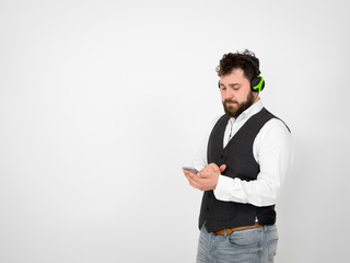 cool man with black beard and white shirt is posing with headphones and smartphone in front of white background
