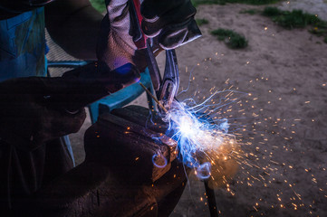 Worker with protective gloves welding metal part in workshop