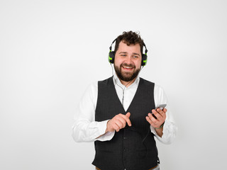 cool man with black beard and white shirt is posing with headphones and smartphone in front of white background