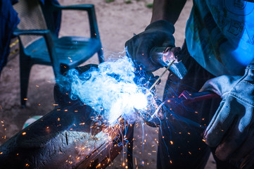 Worker with protective gloves welding metal part in workshop