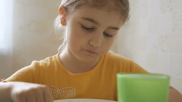 Little girl having Breakfast at home. Pretty American girl eating cereal with appetite. Child having breakfast in the kitchen. Closeup.