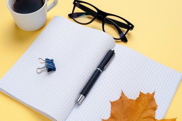 Empty otebook, eyeglasses on yellow background.