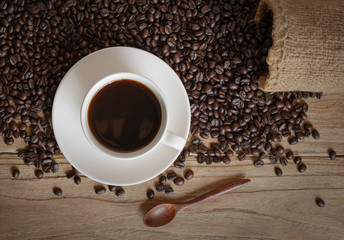 cup of coffee and coffee beans in a sack on wood background, top view