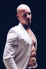 Elegant muscular attractive young man with white smart jacket open on naked torso. Fitness male bodybuilder posing.