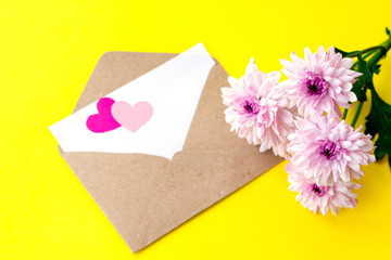 Love envelope with blank letter and pink chrysanthemum flowers with two pink hearts on bright yellow bacground. Copy space