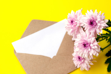 Love envelope with blank letter and pink chrysanthemum flowers on bright yellow bacground. Copy space