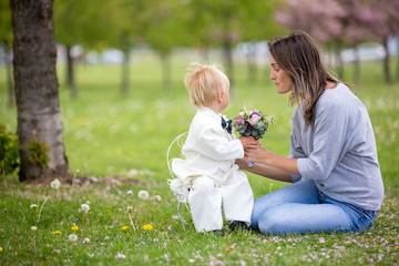 Beautiful toddler boy, dressed in white tuxedo, holding gorgeous flower bouquet for mothers day