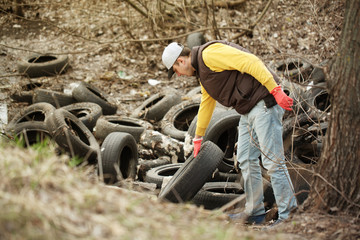 Volunteer removes car tires from the park. Environmental pollution, outdoor trash and rubbish.