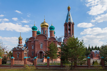 Fototapeta na wymiar A newly built orthodox church of red brick with green and golden domes in the Moscow Region (Russia)