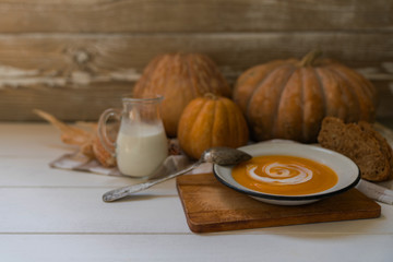 Homemade autumn butternut squash soup with bread. Roasted pumpkin and carrot soup with cream and pumpkin seeds on white wooden background. Concept of healthy eating food. Copy space. Toned image.