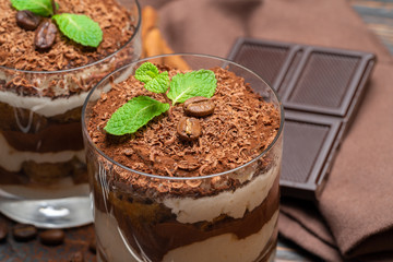 two portions Classic tiramisu dessert in a glass and chocolate bar on wooden background
