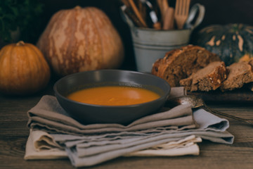 Homemade autumn butternut squash soup with bread. Roasted pumpkin and carrot soup with cream and pumpkin seeds on white wooden background. Concept of healthy eating food. Copy space. Toned image.