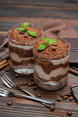 two portions Classic tiramisu dessert in a glass and chocolate bar on wooden background