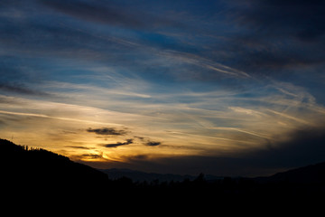 Sunset in a mystic scenery with colorful sunset with different types of clouds and a hill silhouette in the austrian alps in styria