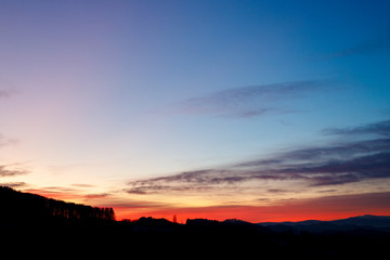 colorful sunset with glowing clouds and a tree a hill and valley silhouette in the austrian alps