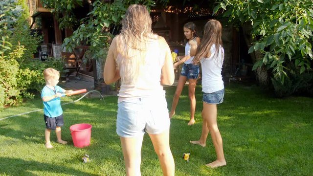 Slow motion video of cheerful young family with children playing with water guns and water hose in garden at hot summer day