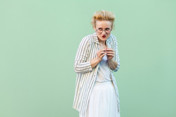 Portrait of funny young blonde woman in white shirt, skirt, and striped blouse with eyeglasses...