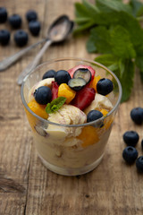 Vanilla ice cream with fruits - blueberries, strawberries, mango and mint, summer refreshing dessert. Wooden background. Glass with vanilla icecream.