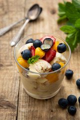 Vanilla ice cream with fruits - blueberries, strawberries, mango and mint, summer refreshing dessert. Wooden background. Glass with vanilla icecream.