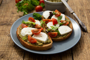 Mozzarella cheese, cherry tomatoes and pesto bruschetta, toast on wooden background. Healthy breakfast ,snack. Pesto pasta.